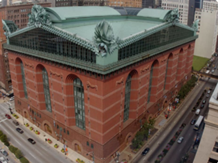 Aerial view of a red-brick building with a green roof and sculptures at a busy urban intersection.