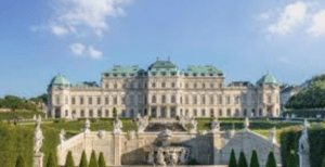Grand historic building with ornate facade, domes, statues, stone terrace, and manicured gardens.