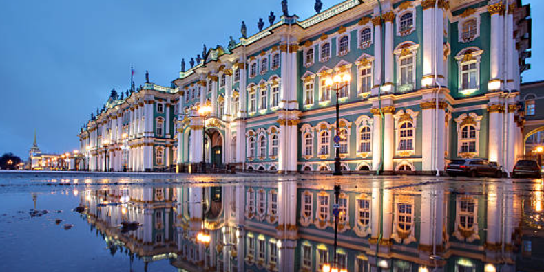 Grand historic building with ornate architecture illuminated at twilight, reflected in a large puddle.