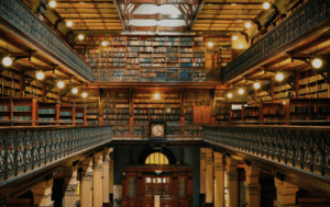Grand multi-tiered library with numerous bookshelves, ornamental railing, clock, and arched doorway
