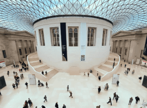 Large indoor space with circular white building, glass and steel roof, people walking and gathering.