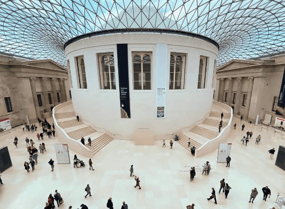 Large indoor space with circular white building, glass and steel roof, people walking and gathering.