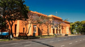 Large orange-painted classical-style building along a tree-lined street on a sunny day.