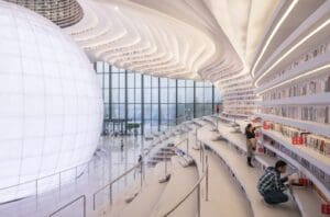 Modern library with large spherical structure, tiered bookshelves, and people browsing books.
