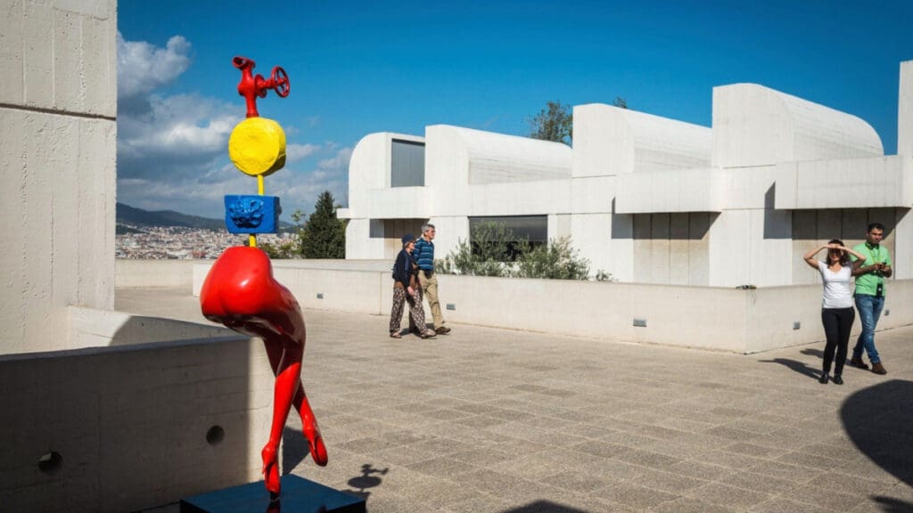 Abstract sculpture and people outside modern white buildings with clear blue sky and cityscape views