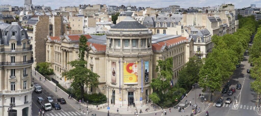 Aerial view of a neoclassical building with banners, at the intersection of tree-lined streets.