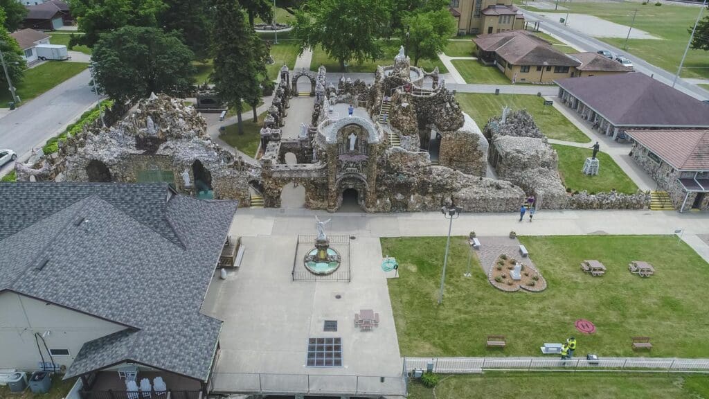 Aerial view of a detailed stone shrine complex with statues, pathways, lawns, buildings, and streets.