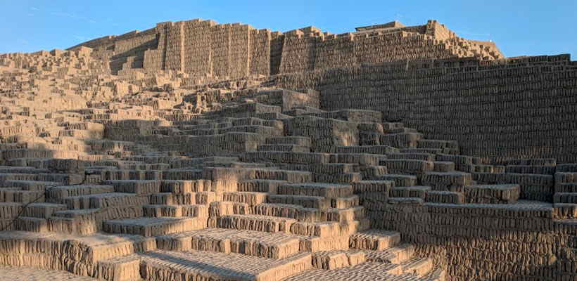 Ancient adobe brick pyramid with terraced levels under clear blue sky. Archaeological site.