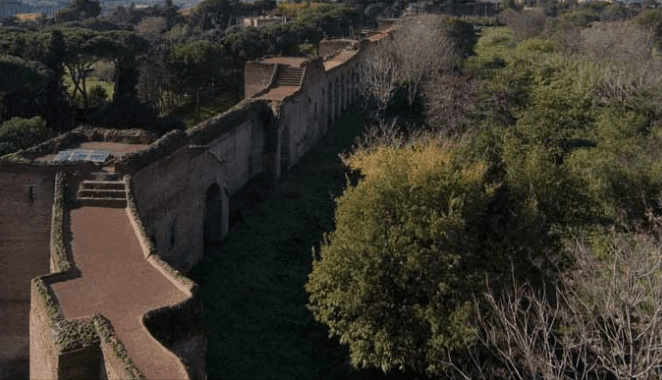 Ancient brick wall extending through a green landscape with trees and a staircase on the left.