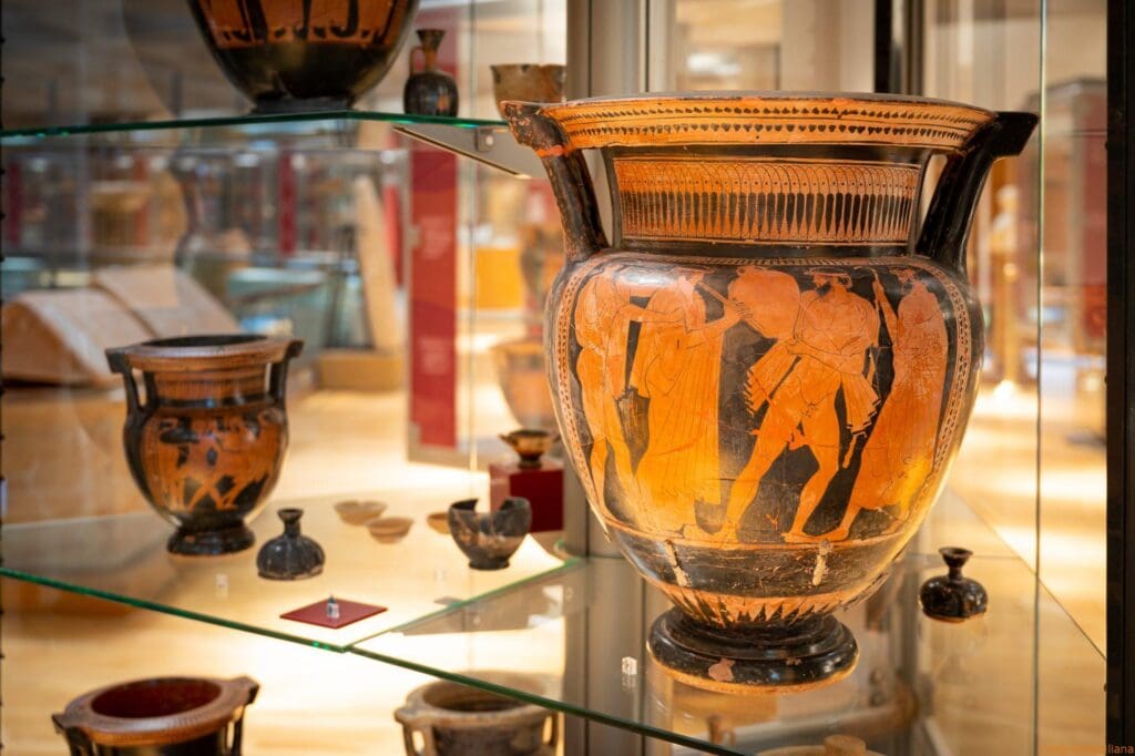 Ancient pottery display with a large amphora depicting human figures, surrounded by smaller ceramics.