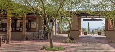Scenic view of Arizona-Sonora Desert Museum sign, walkway with benches, trees, and desert landscape.