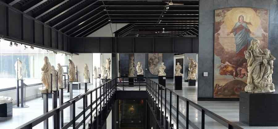 Interior of art gallery with classical sculptures, high ceilings, and large religious paintings.