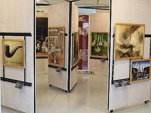 Art gallery interior with movable panels displaying various framed artworks in a zigzag pattern.