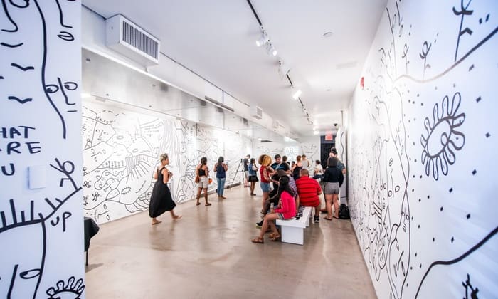 People in an art gallery with large monochrome abstract murals, some observing, others seated.