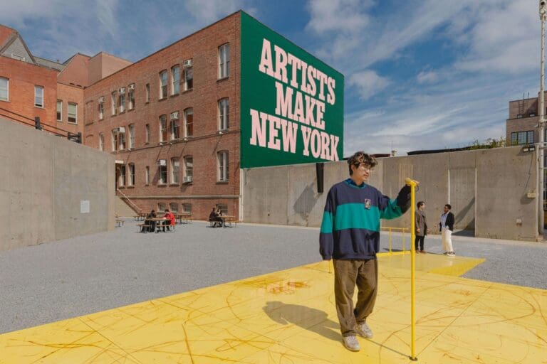 Outdoor art installation with a large "ARTISTS MAKE NEW YORK" sign on a brick building.