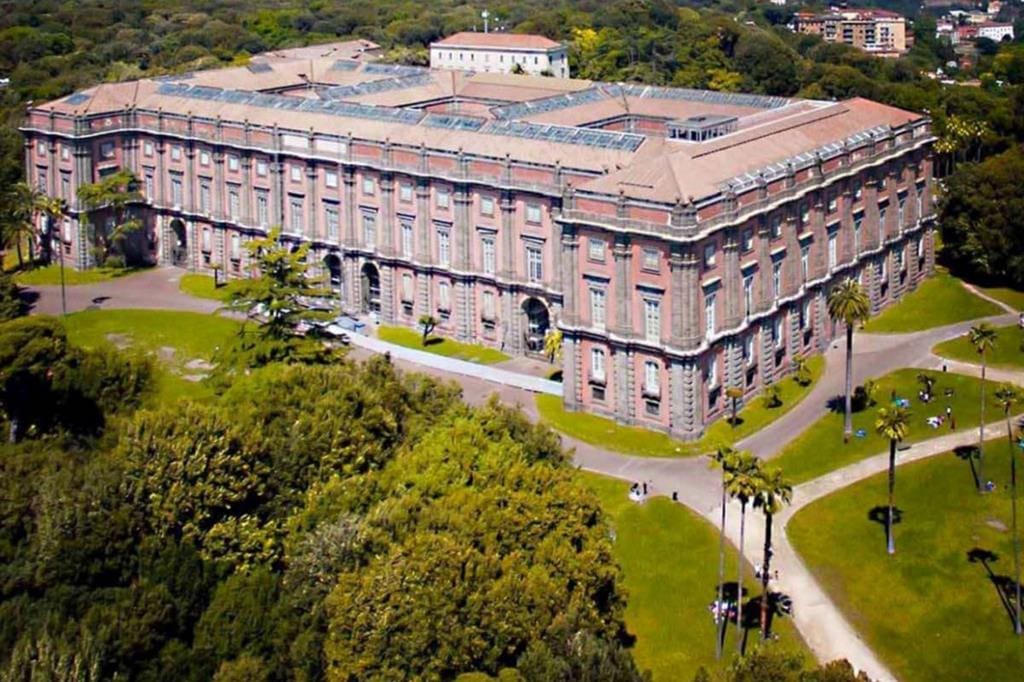 Rectangular brick building with large windows in a green park, featuring skylights and pathways.