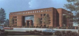 Brick office building with large glass windows, trees, and cars on a nearby road.