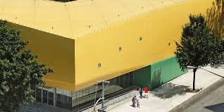 Brightly colored building with yellow upper, green lower, large windows, and trees, viewed from above.