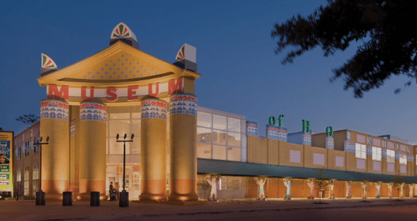 Brightly lit museum with Egyptian-inspired columns, large "MUSEUM" sign, green roof, and trees.
