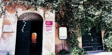 Building facade with two large green wooden doors, one open, showing interior, walls aged beige.