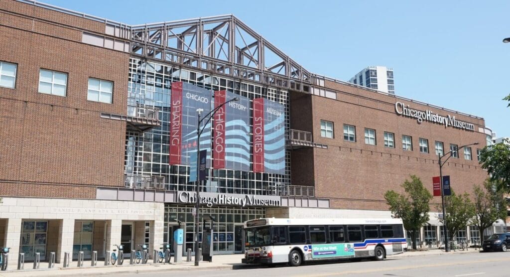 The exterior of the Chicago History Museum with banners and a bus on the street.