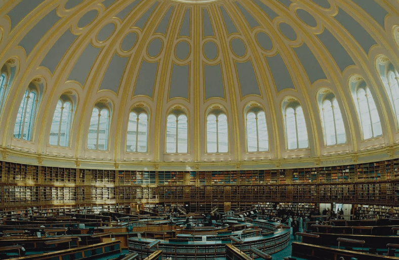 Circular library with a domed ceiling, filled bookshelves, desks, and people reading or studying.