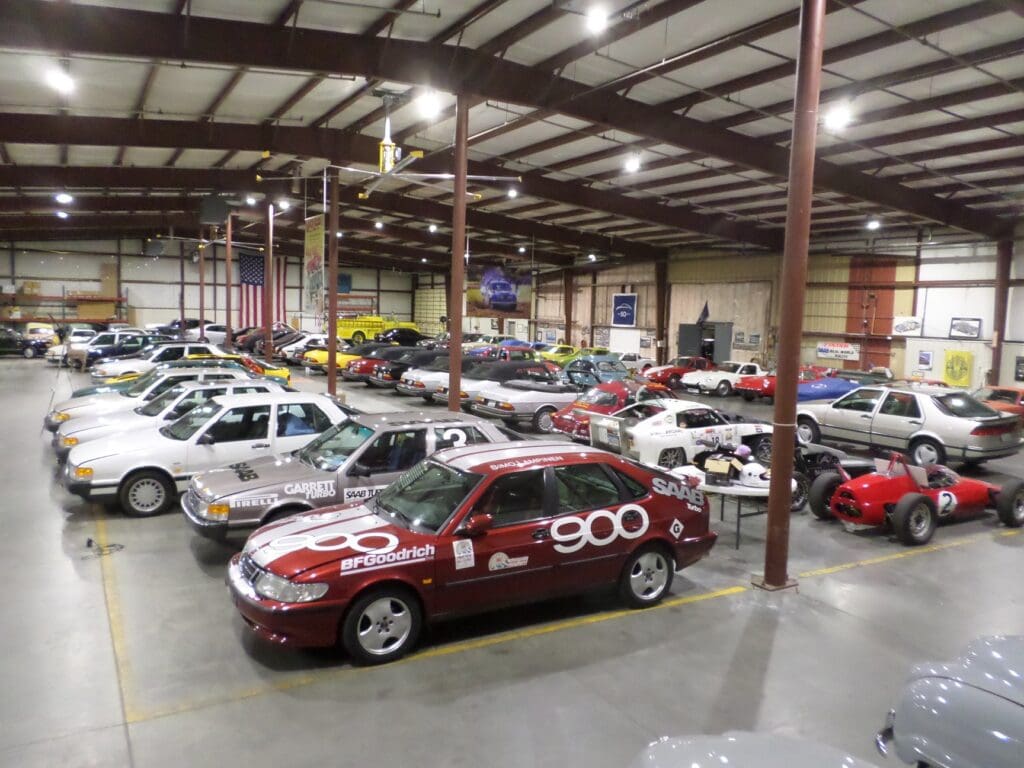 Large indoor garage with various classic cars, race cars, and an American flag in the background.