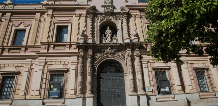 Classical building with arched entrance, statue above door, ornate details, tall windows, and greenery.