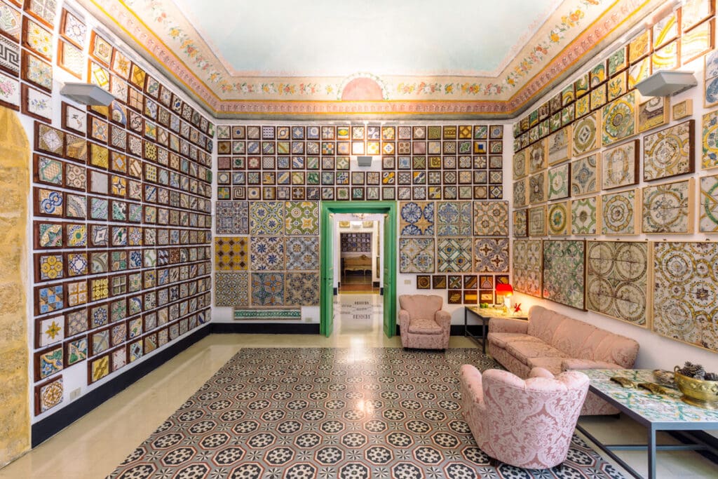 Room with colorful ceramic tiles on walls and floor, pink sofa set, and a green-framed doorway.
