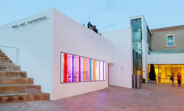 Contemporary art museum with white exterior, colorful window lights, stairs, and glass elevator at dusk