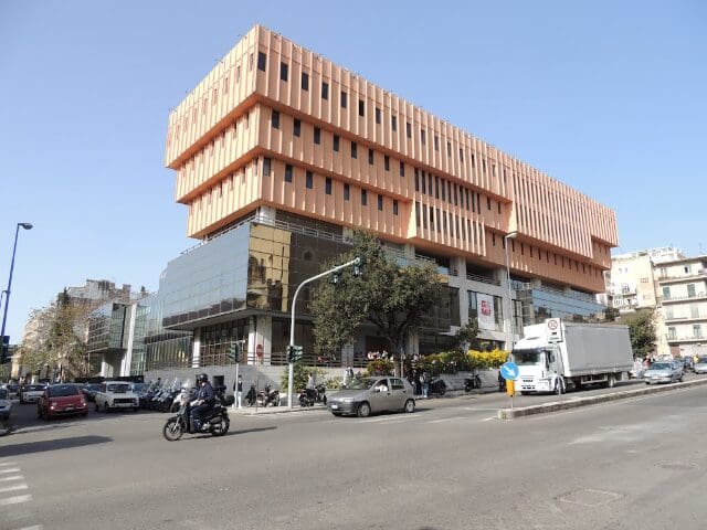Contemporary multi-story building with orange panels and glass at a busy urban intersection.