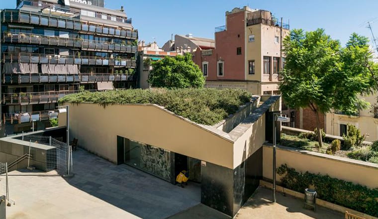 Contemporary building with green roof in an urban courtyard surrounded by older residential structures.