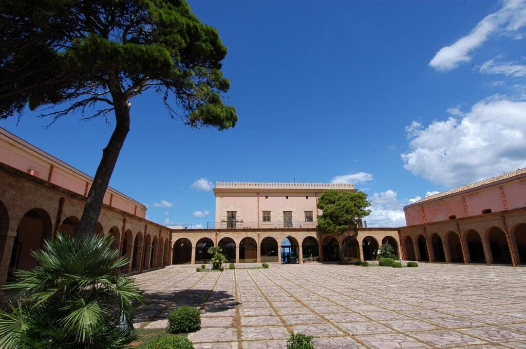 Courtyard with central open space, archways, two-story building, trees, clear sky, and scattered clouds