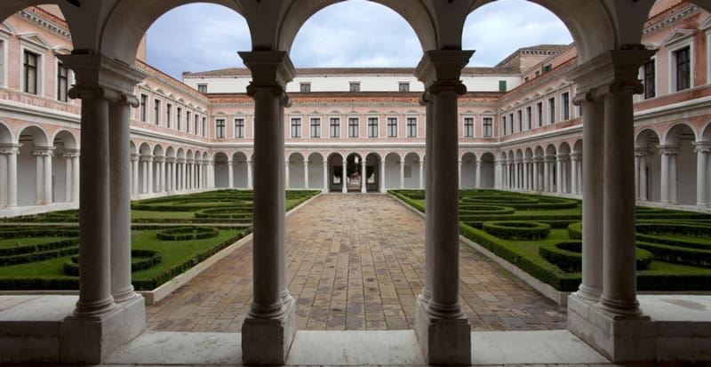 Courtyard with manicured hedges, central walkway, surrounded by a two-story building with arches.