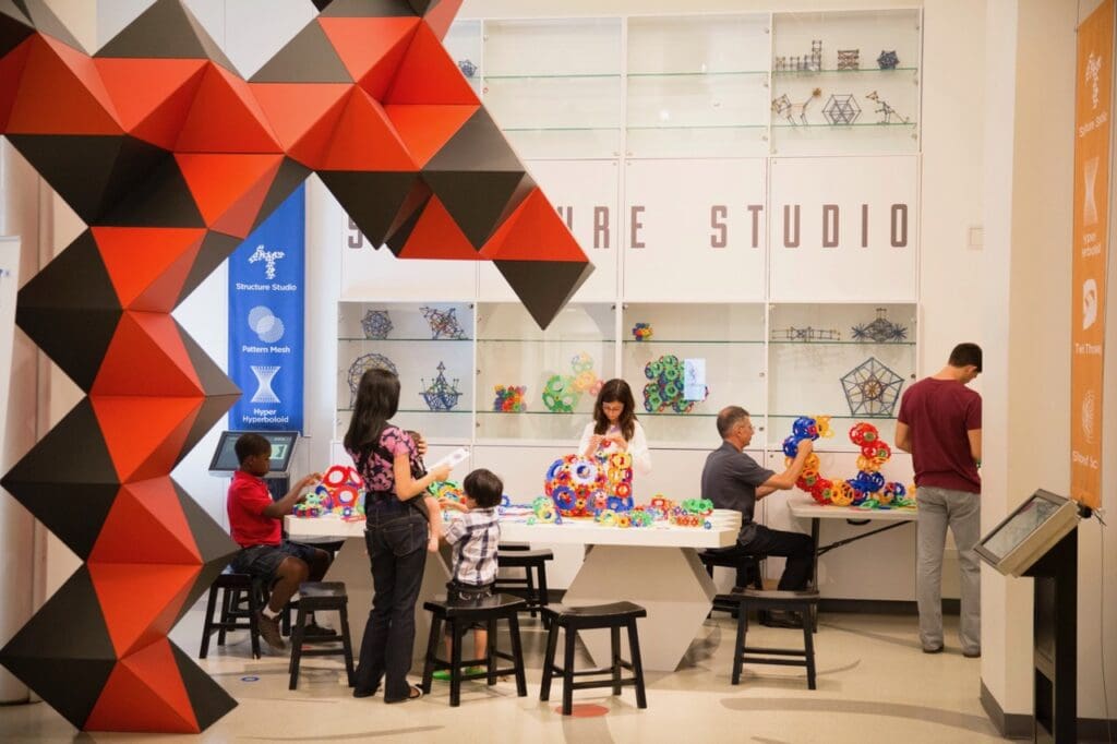 Creative workspace with adults and children building geometric structures at a table labeled 'Structure Studio'.