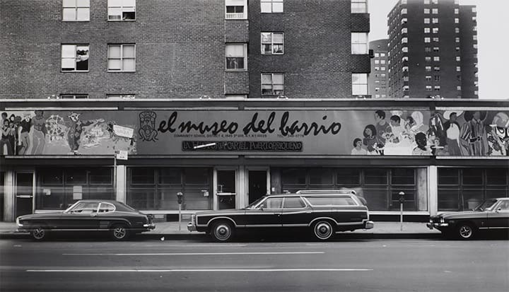 El Museo del Barrio exterior with mural and windows, vintage cars parked in front on street.
