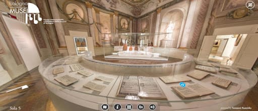 Elegant museum room with circular display case of manuscripts, frescoed ceilings, arched windows.