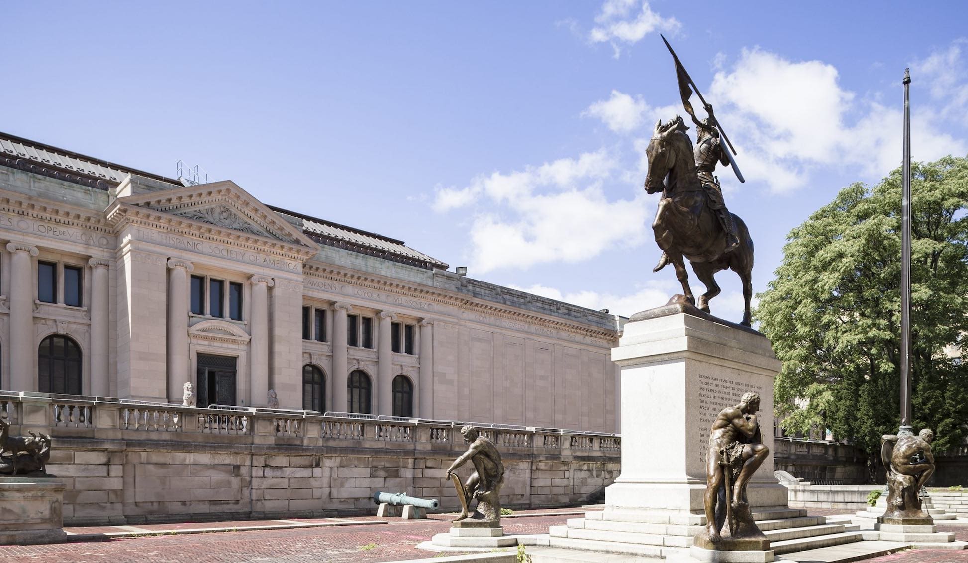 Equestrian statue in front of a historic building with columns, statues, and a tree under blue sky.