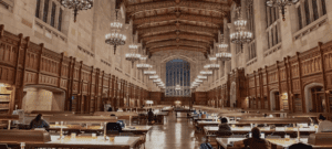 Expansive library interior with chandeliers, arched windows, wooden tables, and ornate details.