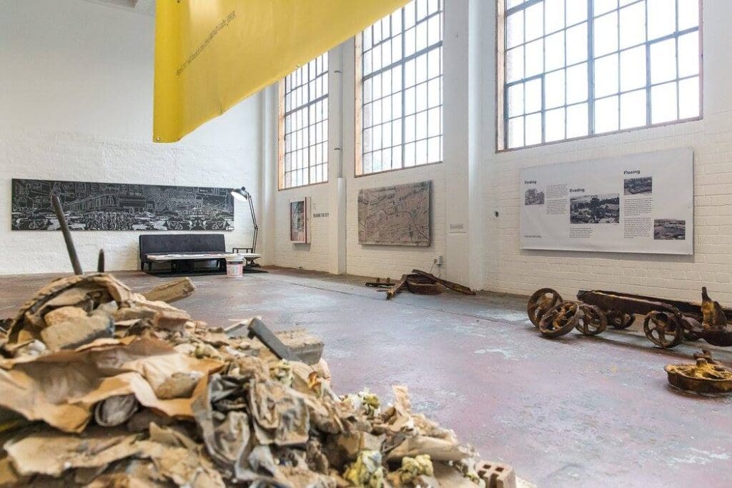 Gallery space with art installations, informational displays, natural light, and industrial decor.