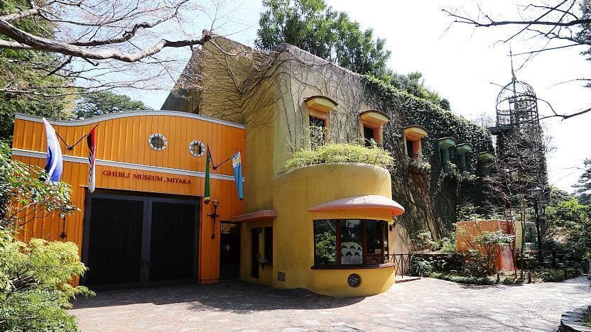 Ghibli Museum in Mitaka, Japan, with yellow-orange facade, greenery, and whimsical architecture.
