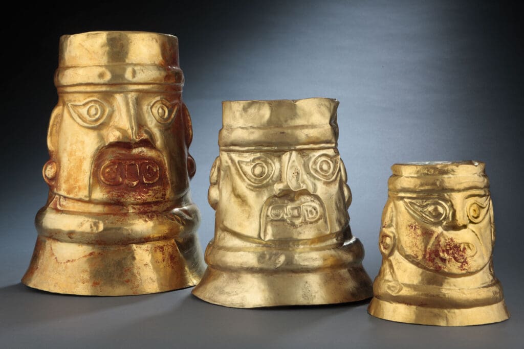 Three gold artifacts resembling stylized human faces, with varying sizes and distinct facial details.