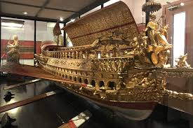 Ornate golden ship model with intricate carvings in a glass exhibition case, museum setting.