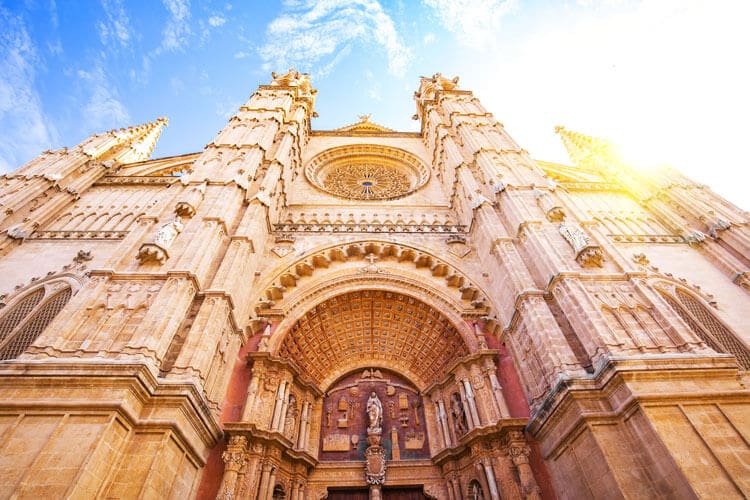 Gothic cathedral exterior with pointed arches, stone carvings, large rose window, and towering spires.