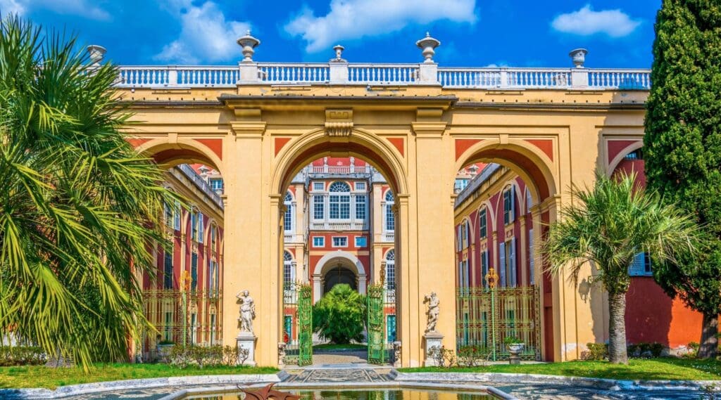 Grand building with arched entrance, classical elements, statues, palm trees, and reflecting pool.