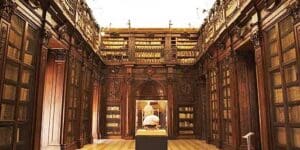 Grand library with wooden shelves, ornate balcony, and central lit display case showcasing an item.