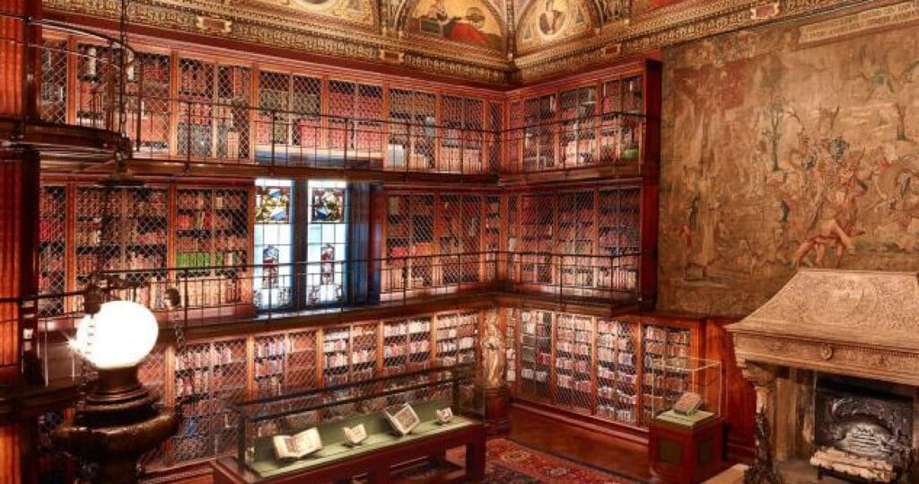 Grand library with wooden shelves, upper-level walkways, stained glass, tapestry, and ornate fireplace.