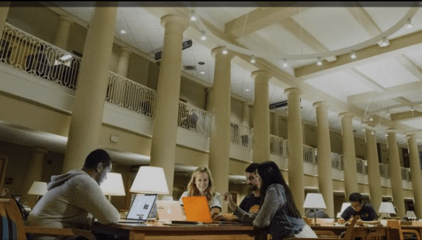 Group at a large wooden table with laptops in a bright, spacious library with tall columns.