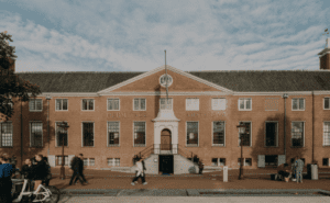 The image shows a red-brick building labeled "Heritage Amsterdam" with people walking and biking in front.