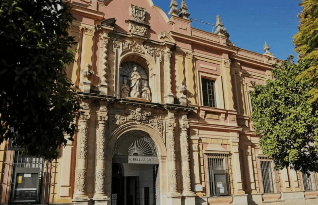 Historic building with arched entrance, carvings, statues, pink and beige facade, "BELLAS ARTES" sign